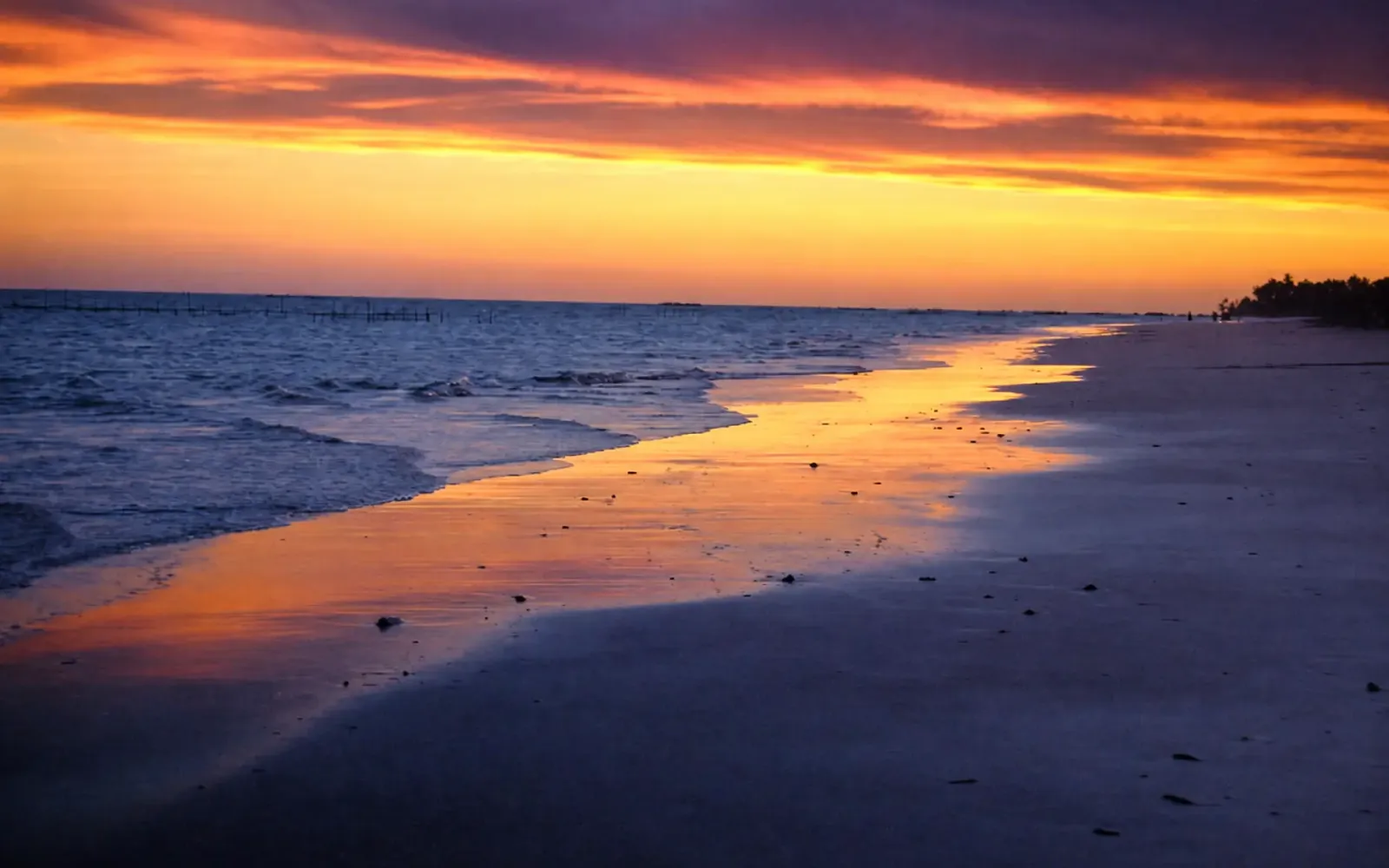 Sunset over the shoreline near Porto da Rua, with reef stakes on the horizon