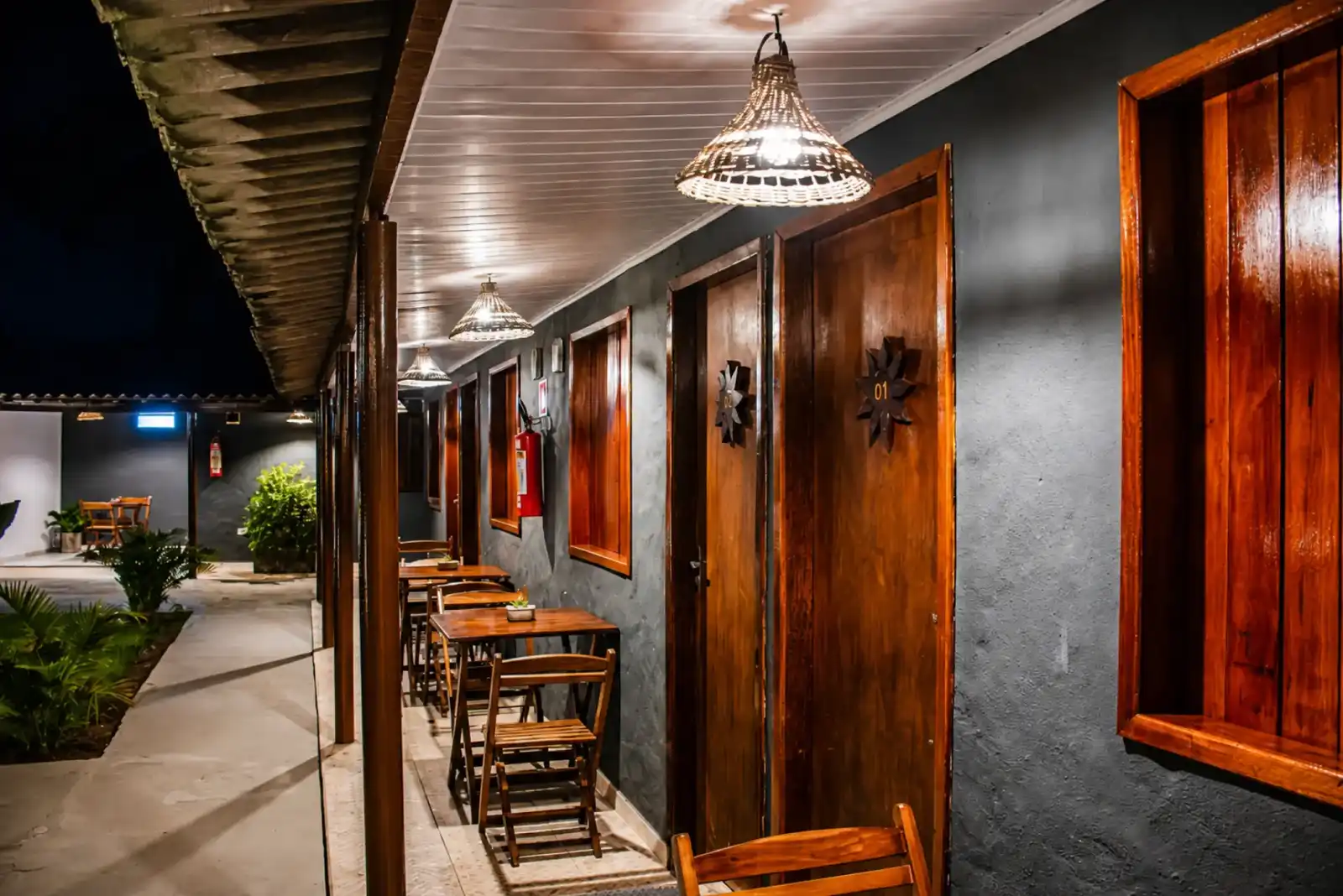 Lit walkway at night past numbered wooden guest room doors and small tables
