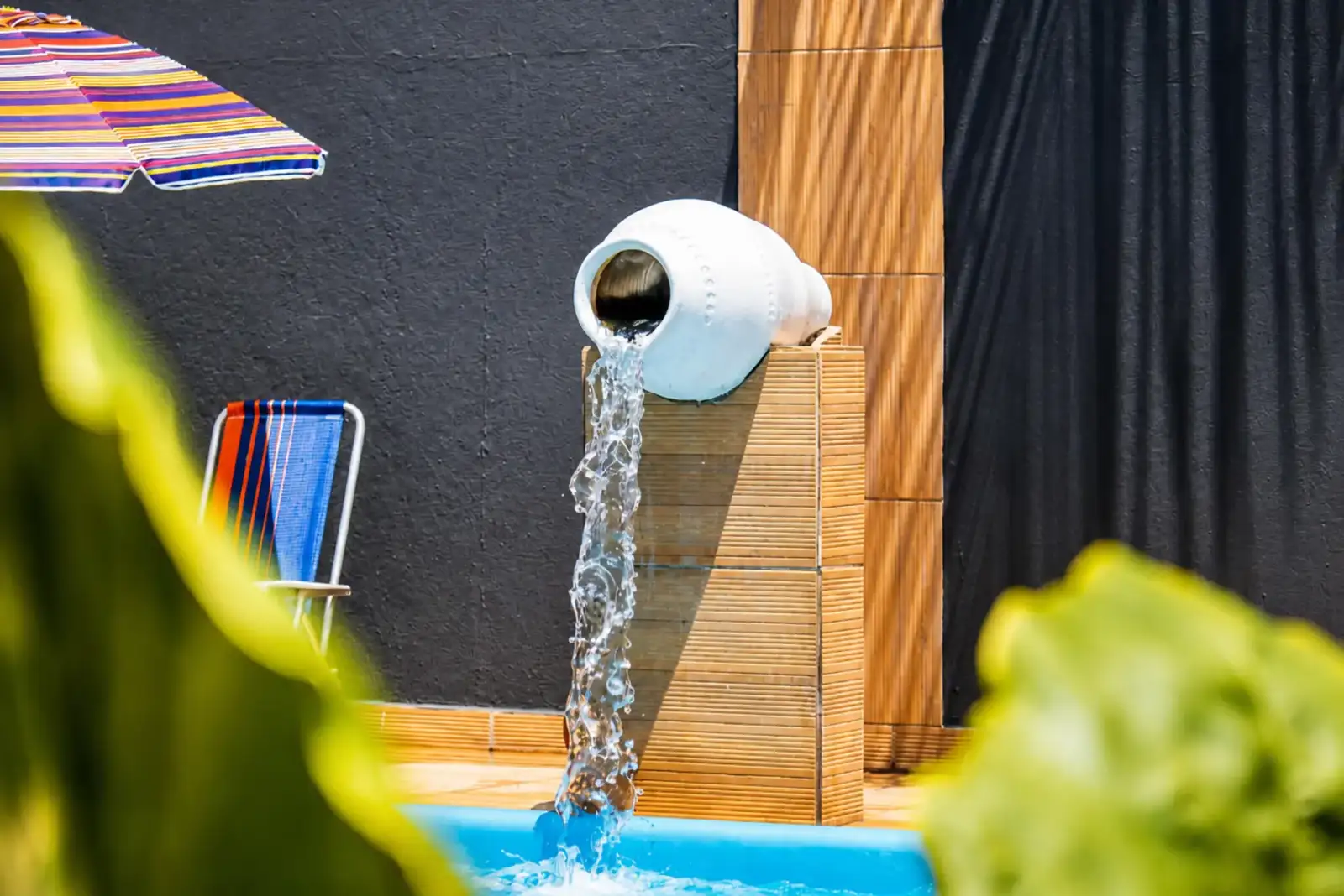 Ceramic jar water feature pouring into the pool, framed by tropical leaves